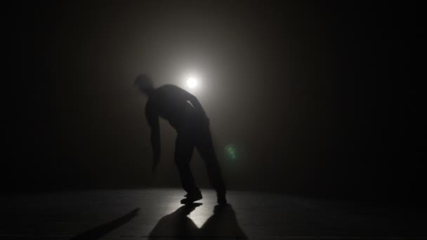 Talented young boy silhouette performing break dancing tricks in front of the spotlight in slow motion — Stock Video