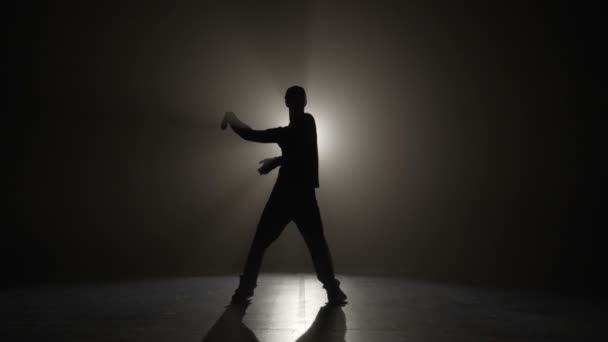 Silueta de cámara lenta de un hombre que usa gorra y realiza movimientos de onda de danza eléctrica en un escenario oscuro antes del concierto — Vídeo de stock