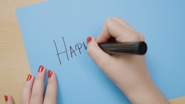 Mädchenhände mit roten Nägeln schreiben auf blauem Papier glücklichen Vatertag mit schwarzem Filzstift — Stockvideo