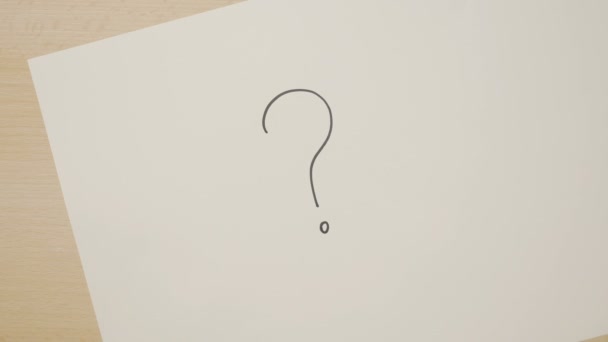 Mãos de uma mulher desenhando vários pontos de interrogação em um livro branco usando um marcador preto — Vídeo de Stock