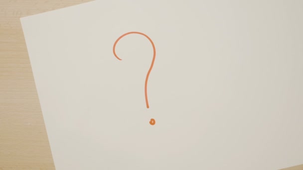 Mãos femininas com unhas vermelhas desenhando muitos pontos de interrogação em um papel branco com um marcador laranja — Vídeo de Stock