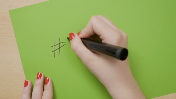 Mujer manos escribiendo hashtag en un papel verde usando un marcador negro — Vídeos de Stock