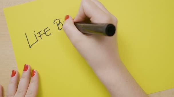 Kvinnliga händer skriver livet börjar efter kaffe på en gul sida med en svart markör — Stockvideo