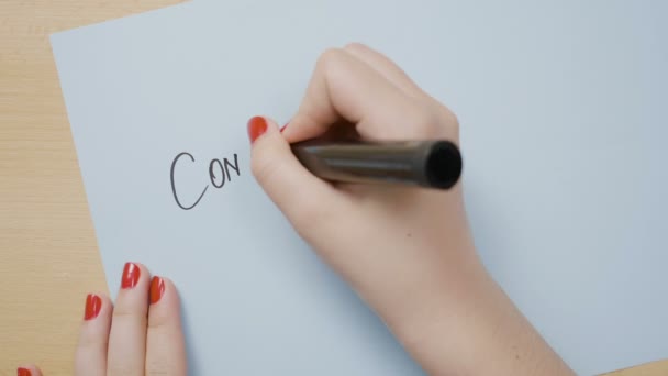 Vrouwelijke handen schrijven gefeliciteerd met een blauw papier met behulp van een zwarte markering — Stockvideo