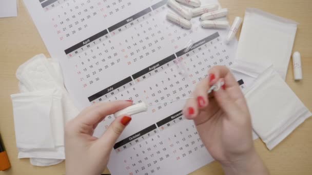 Young vlogger female hands social media influencer with red manicure presenting types of tampons and pads over a calendar on a desk — Stock Video