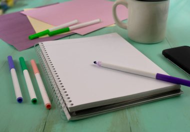 Ahşap masanın üzerine renkli kalemler ve fotokopi alanı olan kahve fincanı olan boş çizim defteri.