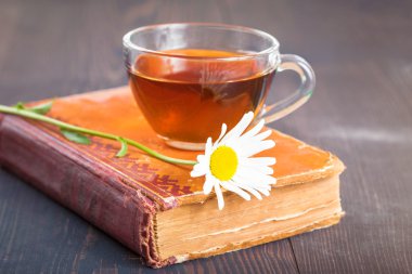 Fincan çay, papatya ve masanın üzerine bir kitap