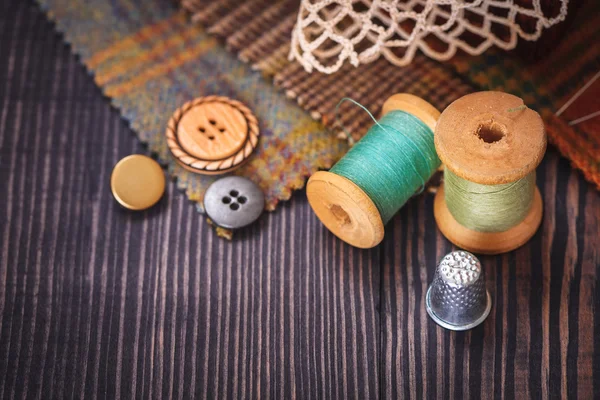 Thimble, buttons, spools of thread and fabric swatches on a wooden background