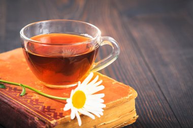 Fincan çay, papatya ve masanın üzerine bir kitap