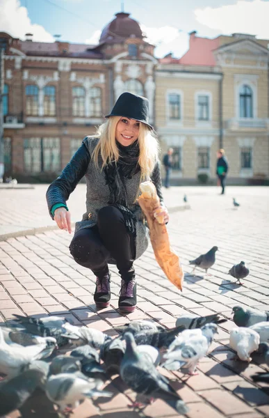 Young beautiful woman is feeding pigeons with bread crumbs in the town square — Stock Photo, Image