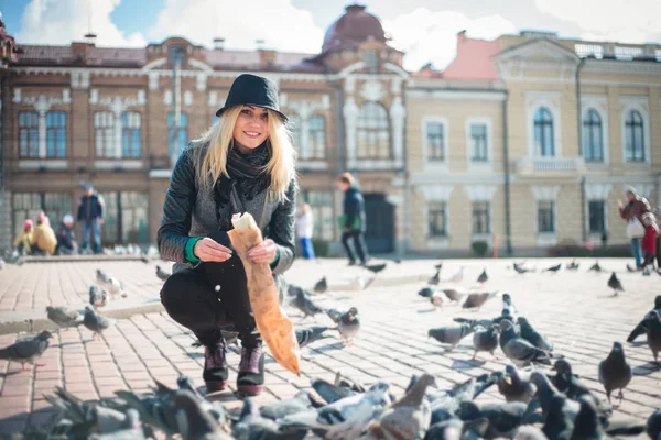 Young beautiful woman is feeding pigeons with bread crumbs in the town square — Stock Photo, Image