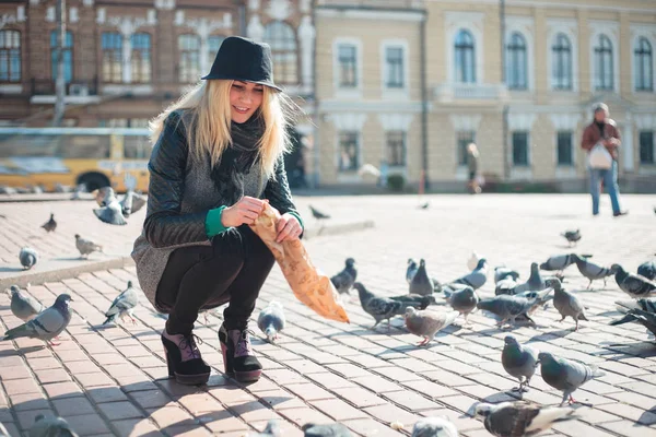 Jeune belle femme nourrit les pigeons avec des miettes de pain sur la place de la ville — Photo