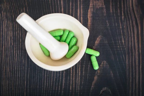 Pharmacy pestle and mortar with green capsules.