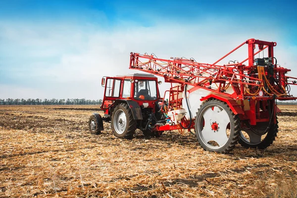 Красный трактор с прицепным распылителем в поле против голубого неба . — стоковое фото