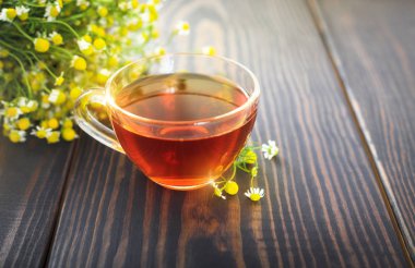 Fincan papatya çayı ve bir demet papatya çiçeği masada.