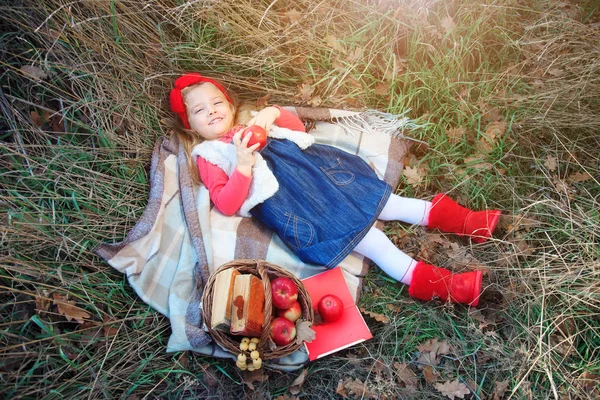 フルーツのバスケットと格子縞の芝生で横になっている少女. — ストック写真