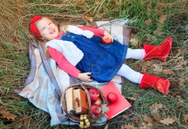 Küçük kız bir ekose meyve sepeti ile çimlere yatan.