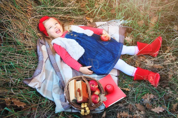 Ragazzina sdraiata in erba su un plaid con un cesto di frutta . — Foto Stock