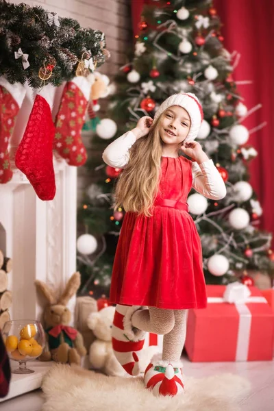 Lovely girl in santa cap near christmas tree, studio shot. — Stock Photo, Image