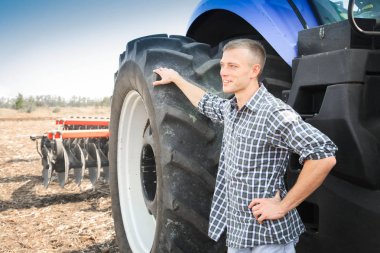 Genç çekici adamın yanına bir traktör. Tarım kavramı.