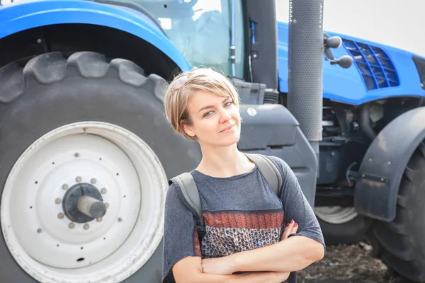 Красивая молодая женщина стоит на заднем плане с трактором — стоковое фото