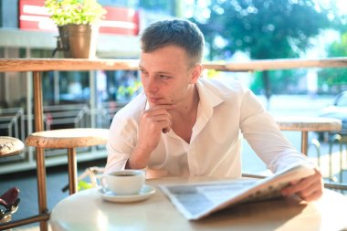 Düşünceli adam öğle yemeğinde sokak bir kafede bir gazete okuyor.