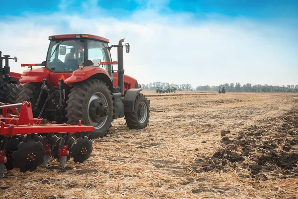 Červený traktor v poli na jasný slunečný den. — Stock fotografie