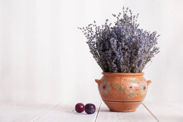 Bodegón con lavanda en una jarra de barro y ciruelas sobre la mesa . — Foto de Stock