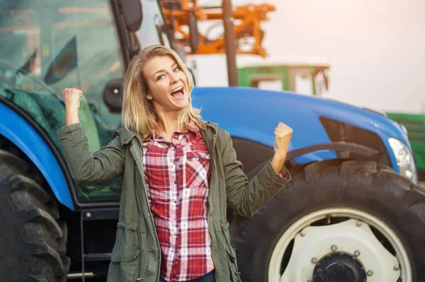 Młoda kobieta z pozytywnymi emocjami w pobliżu traktora. Koncepcja sukcesu w rolnictwie. — Zdjęcie stockowe