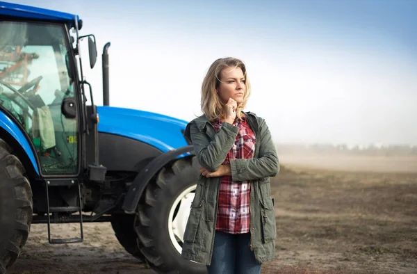 Pensive vrouw in de buurt van de trekker op de achtergrond van het veld. — Stockfoto