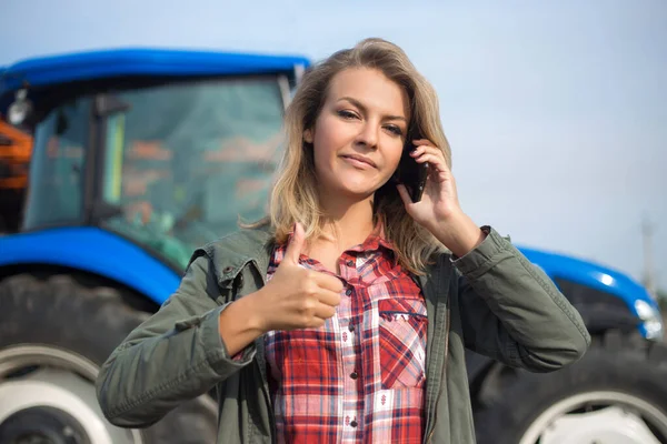 Молодая женщина разговаривает по телефону, задний план трактора с большим пальцем вверх. Концепция успеха, сельского хозяйства . — стоковое фото