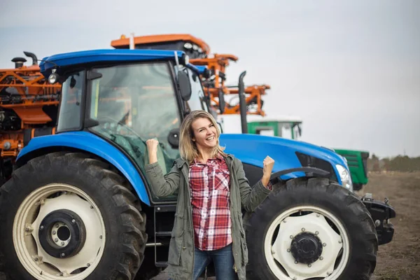 Young woman with positive emotions near the tractor. The concept of success in agriculture.