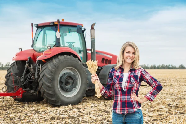 Молодая женщина в поле на фоне трактора с шипом пшеницы в руках . — стоковое фото