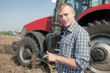 Traktörün yanında elinde tabletle genç bir adam..