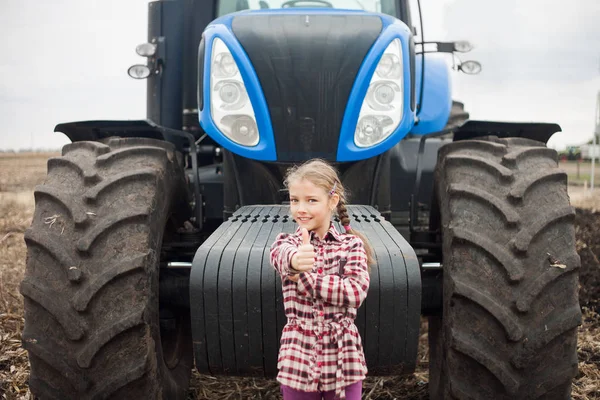 Aranyos lány közel a modern traktor a területen. — Stock Fotó