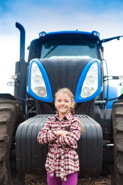 Roztomilá dívka v blízkosti moderního traktoru v terénu. — Stock fotografie