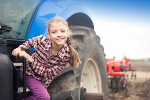 Menina bonito perto do trator moderno no campo . — Fotografia de Stock