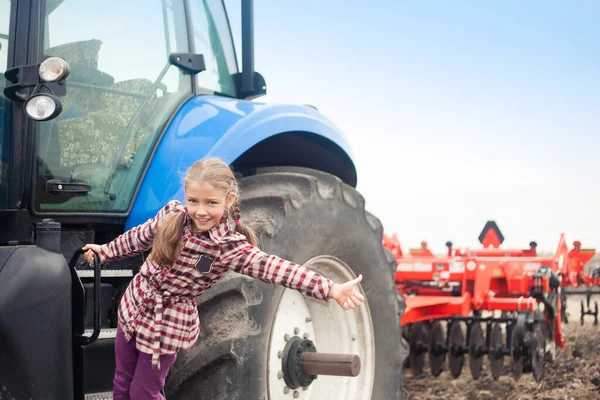 Menina bonito perto do trator moderno no campo . — Fotografia de Stock