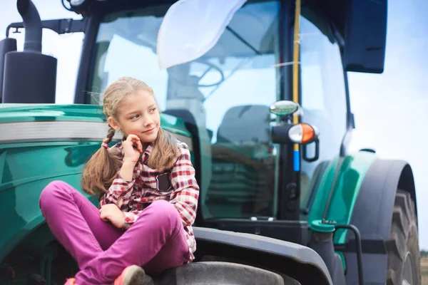 Menina bonito perto do trator moderno no campo . — Fotografia de Stock