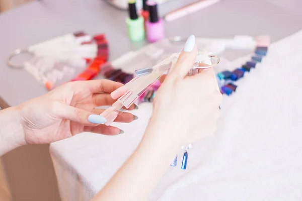 Young woman hands choosing nail color. Female manicured hands and nail color samples, beauty salon.