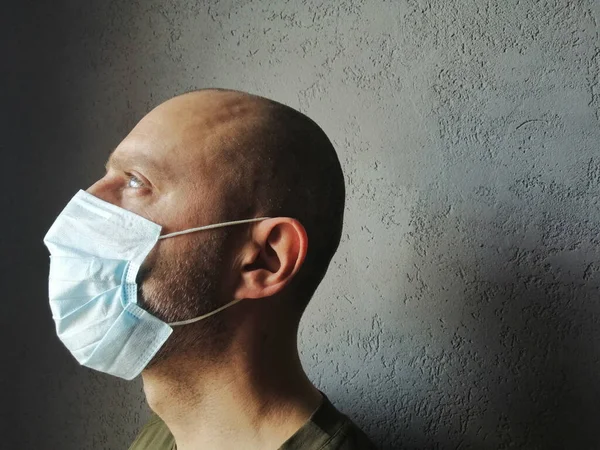 Profilde maskeli bir adam yukarı bakıyor. Covid-19. Korunaklı tıbbi maskeli genç bir adam gri bir arka planda tek başına. salgın, koronavirüs - metin için yer