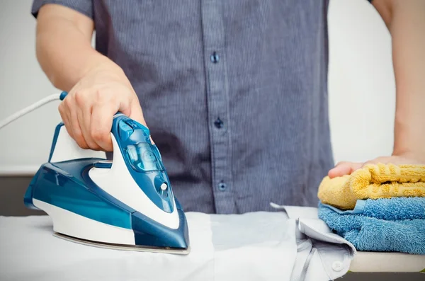 Hombre plancha ropa en tabla de planchar con hierro azul — Foto de Stock