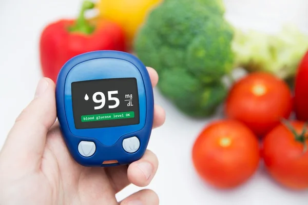 Diabetes doing glucose level test. Vegetables in background — Stock Photo, Image