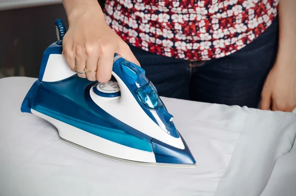 Woman irons clothes on ironing board with steaming iron
