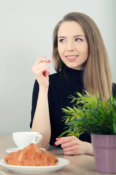 Женщина сидит за столом с кофе и круассаном — стоковое фото