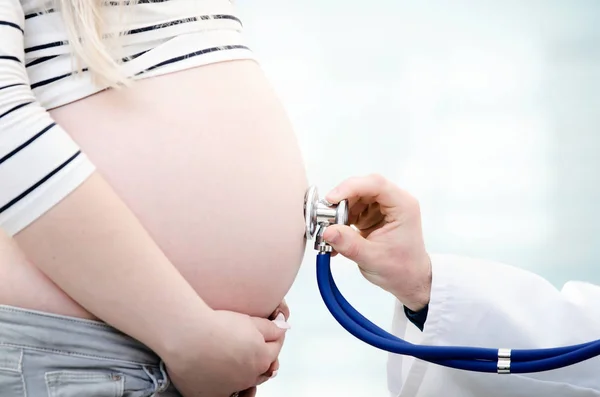 Médico usando estetoscópio examinando mulher grávida — Fotografia de Stock