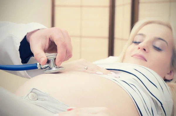 Médico usando estetoscopio examinando mujer embarazada — Foto de Stock