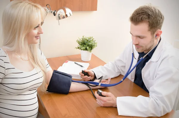 Médico joven comprobando la presión arterial del paciente femenino — Foto de Stock