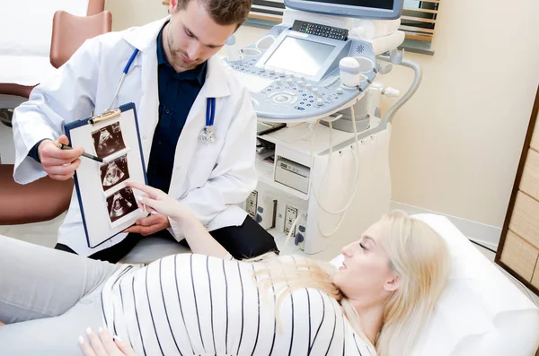 Médico mostrando imagen de ultrasonido de bebé a mujer embarazada . — Foto de Stock