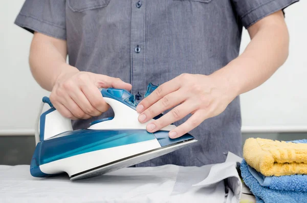 Man irons clothes on ironing board with blue iron — Stock Photo, Image